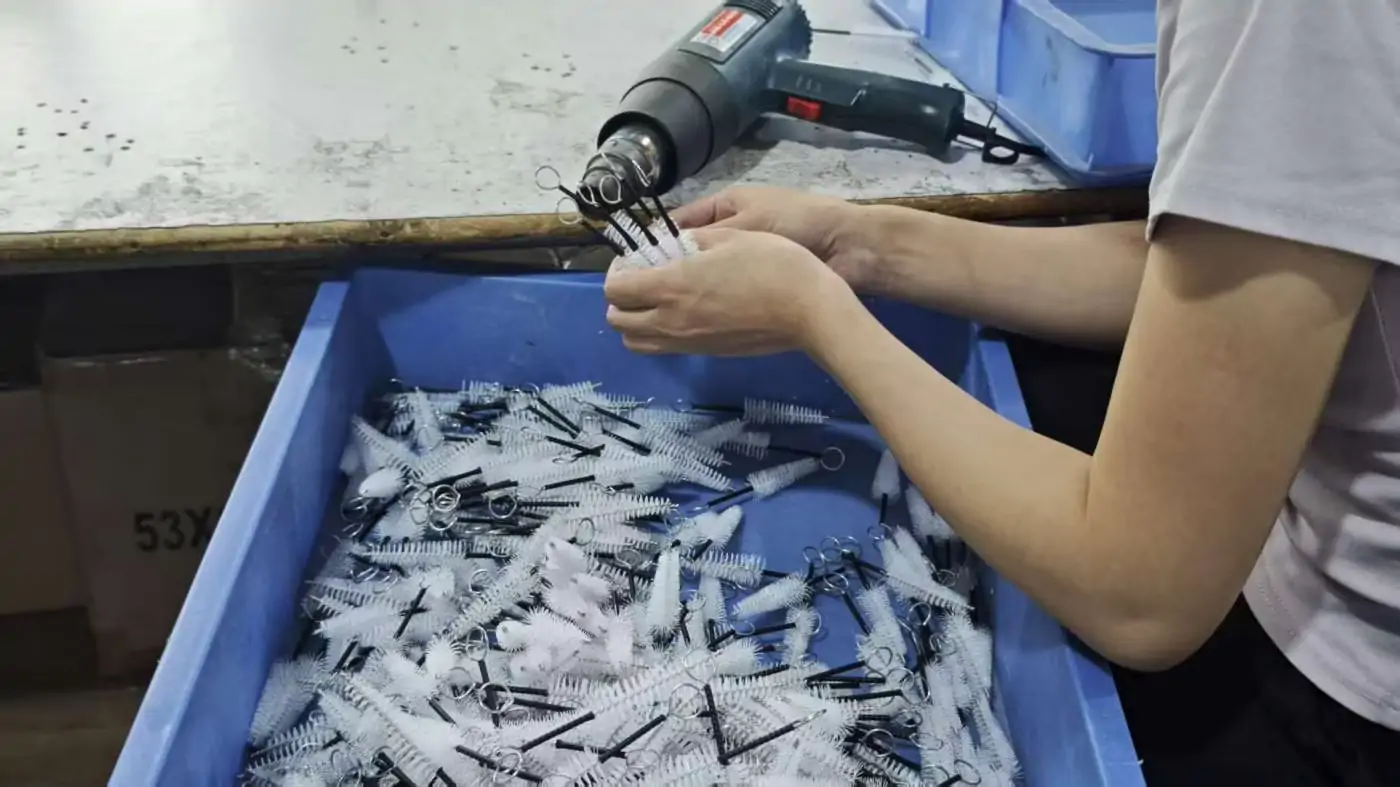 Twisted wire cleaning brushes being assembled and finished on a brush manufacturing production line.